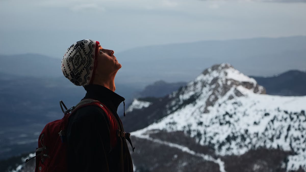A man enjoys a moment of tranquility while hiking in a snowy mountainous landscape.